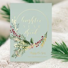 a christmas card with holly and berries on it next to pine cones, greenery and evergreen leaves