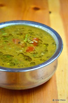 a metal bowl filled with green soup on top of a wooden table next to a spoon