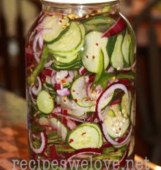 a mason jar filled with sliced cucumbers and red onions sitting on a table