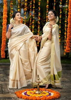 two women standing next to each other in front of an orange flower arrangement and holding hands