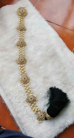 a white rug with a black tassel on top of it and a gold beaded necklace