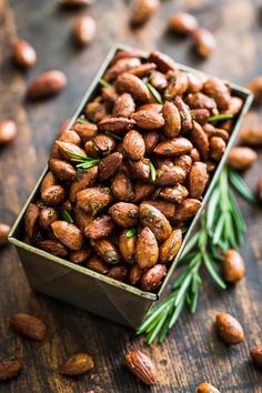 a tin filled with almonds and rosemary sprigs on top of a wooden table