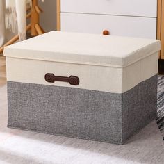 an upholstered storage box sits on the floor in front of a white dresser