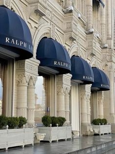 the facade of a building with blue awnings and white planters in front