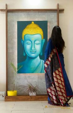 a woman standing in front of a painting with a buddha head on it's face