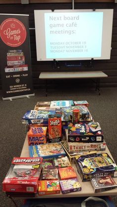 a table topped with lots of books on top of a carpeted floor next to a projector screen