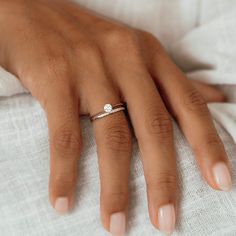 a woman's hand with a diamond ring on top of her finger, resting on a white blanket