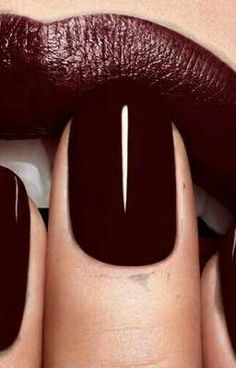 a woman's hands with dark colored nails and maroon lipstick