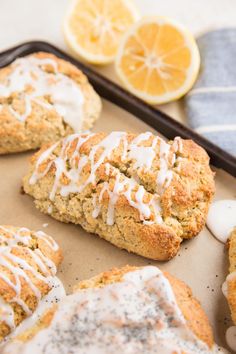 lemon poppy seed scones with icing on a baking sheet next to sliced lemons