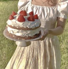 a woman in a dress holding a cake with strawberries on it and smiling at the camera