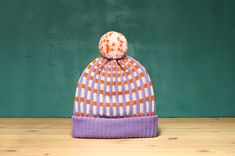 a purple and orange hat sitting on top of a wooden floor next to a green wall