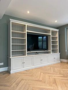 an empty living room with white bookcases and a flat screen tv on the wall