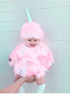 a person holding a child wearing a pink cloud costume with a unicorn horn on it's head