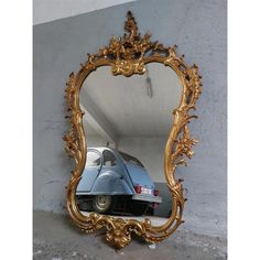 a blue car is in the reflection of a gold framed mirror that hangs on a wall