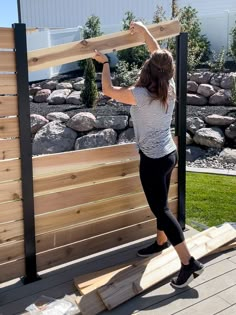 a woman holding up a piece of wood on top of a wooden deck