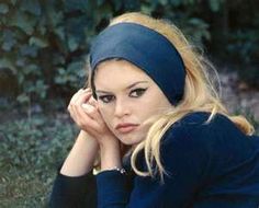 a woman sitting in the grass with her hand on her head and looking at the camera