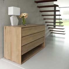 a vase with flowers sitting on top of a wooden dresser next to a stair case