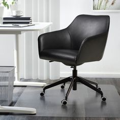 a black office chair sitting on top of a hard wood floor next to a white table