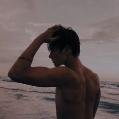 a man standing on top of a beach next to the ocean holding his hand over his head