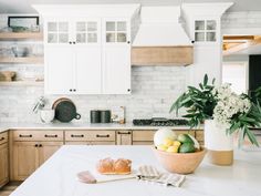 a white kitchen with marble counter tops and wooden cabinets, along with a bowl of fruit