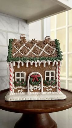 a gingerbread house decorated with icing and candy canes on a cake stand