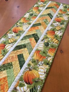 the table runner has pumpkins on it and green, yellow, orange, and white