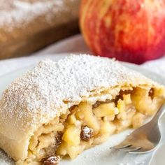 an apple pie with powdered sugar on top sits on a plate next to some apples