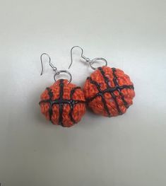 two orange and black balls are hanging from silver earwires on a white surface