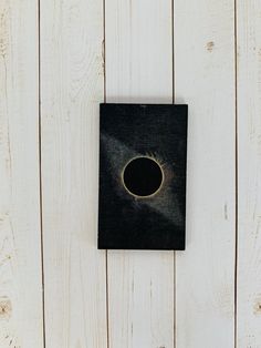 a black square with a hole in the middle on a white wooden wall, surrounded by wood planks