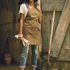 a woman standing in front of a wooden door wearing an apron and holding a pair of gloves