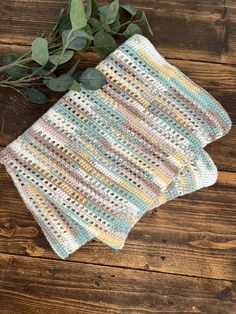 two crocheted dishcloths sitting on top of a wooden table next to green leaves