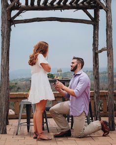 a man kneeling down next to a woman in front of a gazebo with flowers