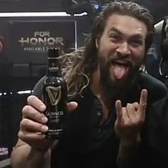 a man with long hair and beard holding up a bottle of beer in front of him