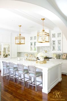 a large kitchen with white cabinets and gold chandelier hanging from the ceiling over an island