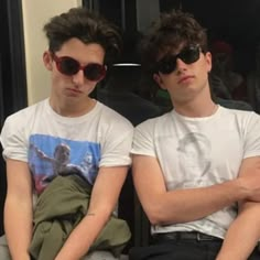 two young men sitting next to each other with their arms crossed and one wearing sunglasses