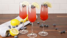 two wine glasses filled with blueberries and lemons on a wooden table next to sliced lemons