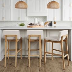 two wooden stools sitting in front of a kitchen island with white cabinets and counter tops