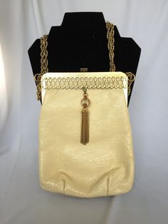 A stunning, vintage clutch/evening bag. This bag is made by Triangle New York, and was made in the 1940s. It is rectangle shape with rounded corners. The body of the bag is an ivory patent leather. It has a gold tone frame that has a wonderful, oval chain link design on the front. And the best part, is a gold tone ball and tassel that sways in the front. The lining is a navy corduroy with a gold lined inner pocket. This bag has a snap clasp and a gold chain strap, that can be worn long or double Classic Cream Rectangular Evening Bag, Cream Rectangular Shoulder Bag For Evening, Cream Rectangular Shoulder Bag For Evenings, Cream Rectangular Shoulder Bag For Formal Occasions, Classic Cream Shoulder Bag For Evening, Classic Beige Evening Bag, Formal Cream Rectangular Shoulder Bag, Cream Clutch Shoulder Bag For Evening, Retro Rectangular Evening Bag For Formal Occasions