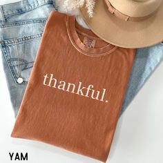 a t - shirt that says, thankful on it next to jeans and a hat