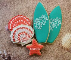 three decorated cookies with seashells and starfish on the sand next to shells