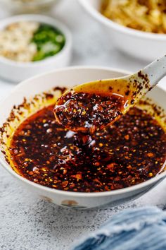 a spoon full of chili sauce in a white bowl with other bowls behind it on a table