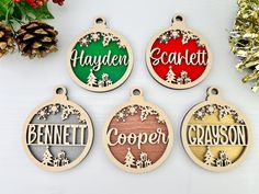 four personalized christmas ornament hanging on a white table next to pine cones