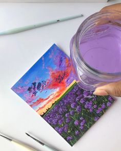 a person holding a purple liquid in their hand and some pictures on the table next to them