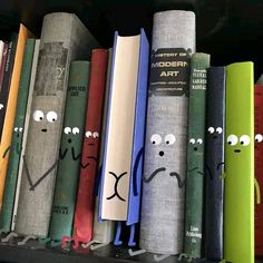 a row of books with faces drawn on them in front of a book shelf filled with books