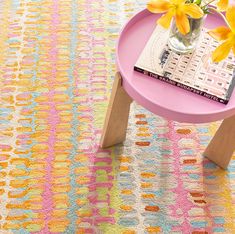 a pink table with yellow flowers in a vase on top of it and a book