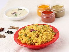 a red plate topped with rice next to bowls of spices and condiments on a white table cloth