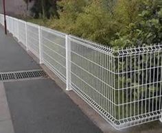 a white metal fence next to a sidewalk with trees and bushes in the back ground