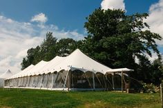 a large white tent set up on top of a lush green field next to trees