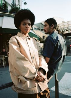 a man and woman standing next to each other on the street with their arms crossed