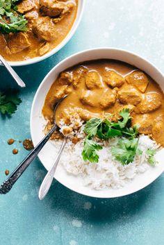 two bowls filled with meat and rice on top of a blue tablecloth next to silver spoons